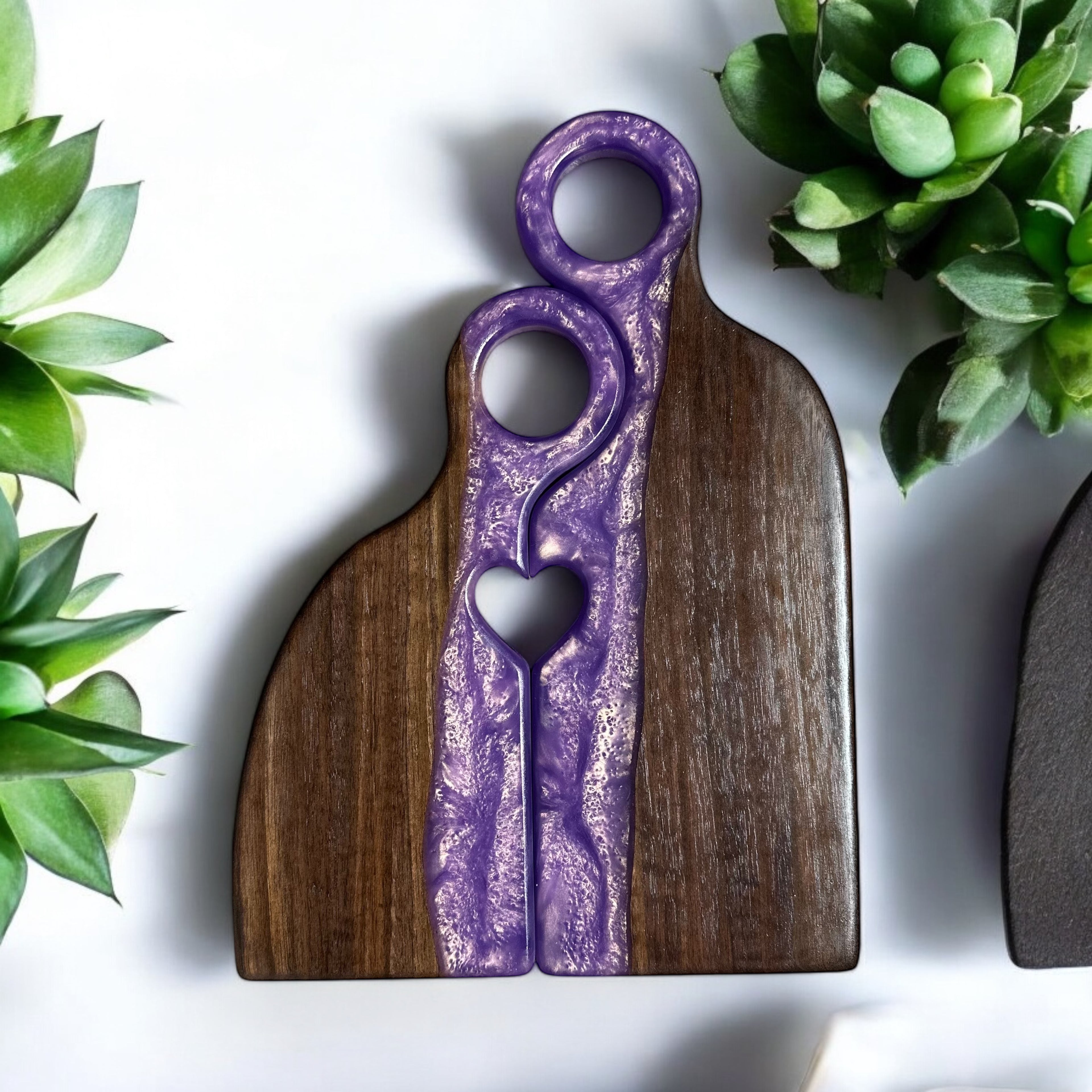 A purple and black resin board with a grooved design, placed on a white surface with a potted plant and a smaller, similar board in the background. Handmade by madera1819, customiizable.