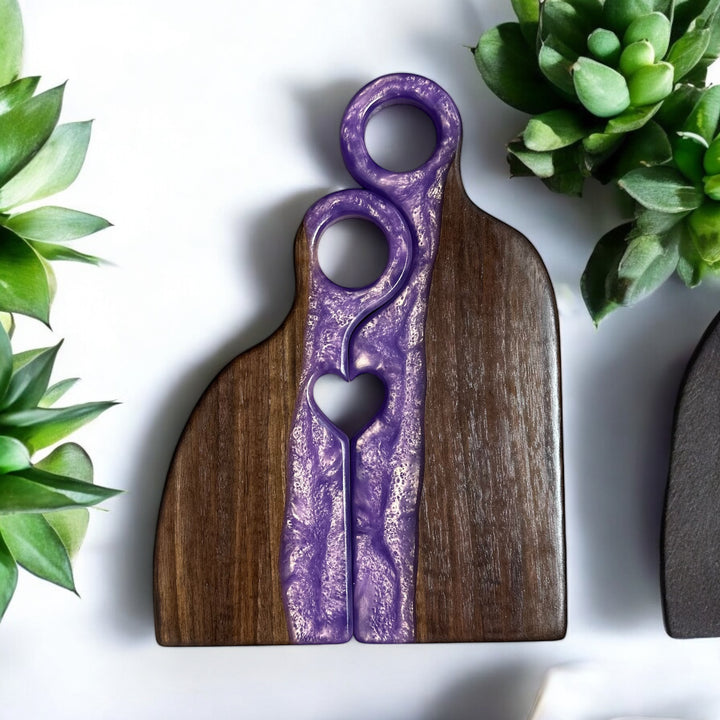 A purple and black resin board with a grooved design, placed on a white surface with a potted plant and a smaller, similar board in the background. Handmade by madera1819, customiizable.